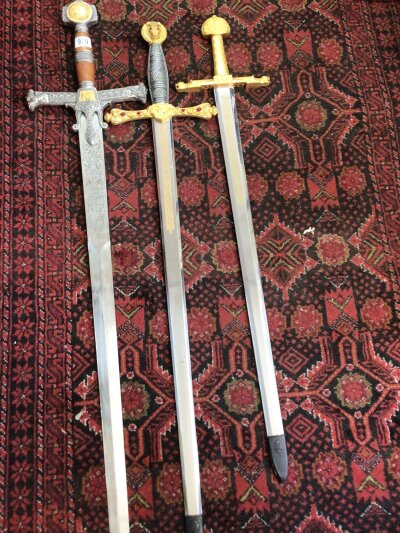Three ornate blunt edged Replica swords with patterned blade decoration and elaborate grips and cross bar. length 120cm