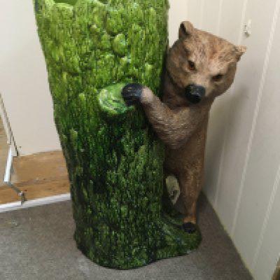 A Bretby stick stand in the form of a bear beside a tree trunk .
