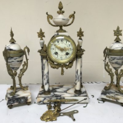 A French late 19th century marble clock garniture of Neo classical design with gilt metal mounts the four pillar clock with an enamel dial with key and pendulum and small feet. 40cm height.