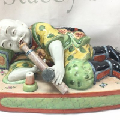 A 19th century Chinese porcelain figure of a sleeping opium smoker, with enamelled flower and Zhou motifs to garments. 15cm tall 32cm wide .this lot cannot be posted