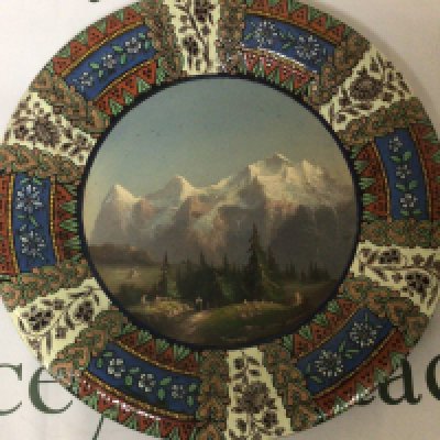A quality ceramic Continental wall plaque hand painted with Tyrollean view with snow caped mountains and figures signed and with makers name to the reverse no obvious damage. 39cm wide.