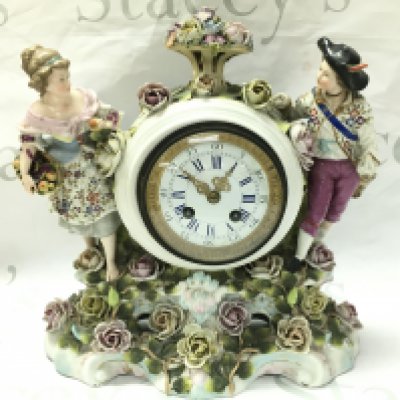 A porcelain clock with raised figures, encrusted with flowers . French movement. Hand missing. Male figures head is damaged. 32cm tall 30cm wide