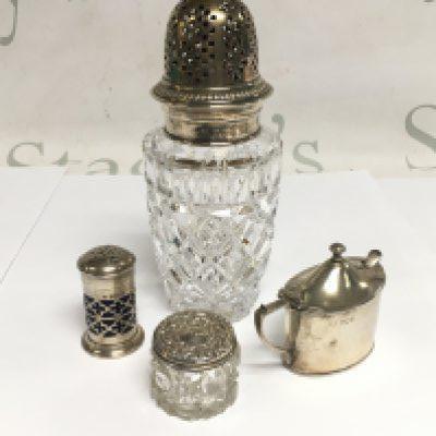 A silver topped sugar caster, silver pepper pot, silver mustard pot and spoon and a silver topped cut glass pot (4). Shipping category D.
