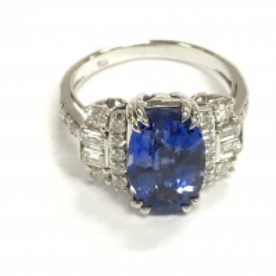 18ct white gold ring set with oval blue sapphire flanked by baguette and round cut diamonds in terraced sides and shoulders. Sapphire 4.65ct and diamonds 0.77ct. Size O