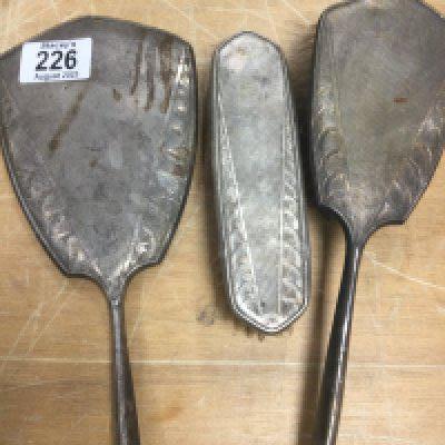 A three piece silver dressing set including a mirror and two brushes.
