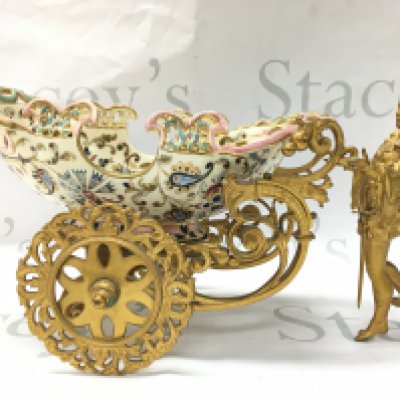 A carriage cachepot centrepiece bowl, gilted figure leading a boat shaped carriage with hand painted and gilted decoration and pierced border. Approximately 18cm tall 35cm long . Stored in a red velvet fitted case . This lot cannot be posted