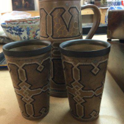 A Doulton jug with a silver plated rim and a pair of matching beakers .