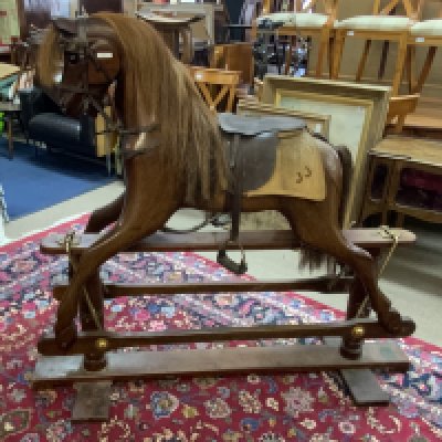 A large carved mahogany rocking horse with leather saddle and horse blanket, in need of attention. 129cm x 147cm x 47cm.