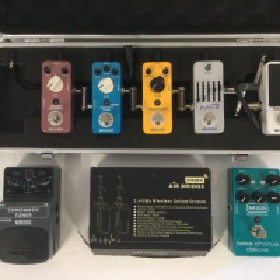 A collection of guitar pedals comprising an MXR bass chorus deluxe, various Mooer pedals, a Behringer tuner and a boxed Air Bridge wireless guitar system.