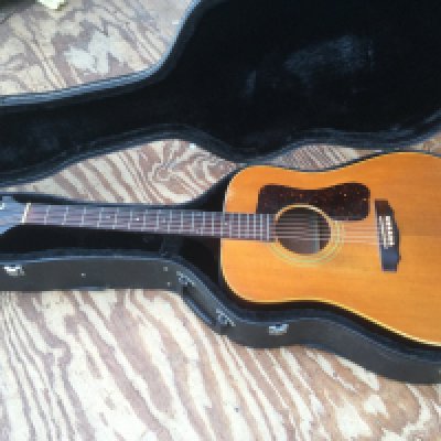 A Guild D40 NT acoustic guitar. Evidence of thorough playwear to the neck and body. Serial number DC100577. Comes supplied with a hard carry case.