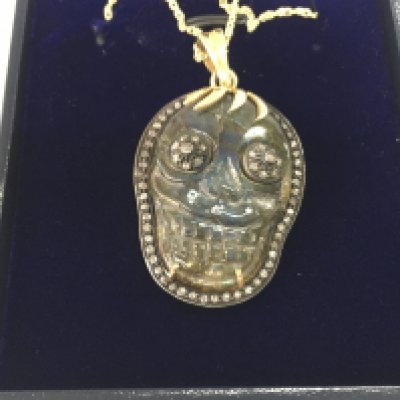A large skull pendant in yellow metal with rose cut diamond set into a carved labradorite on a gold plated silver chain. Labradorite 37.55 and diamonds 0.81ct. Postage B