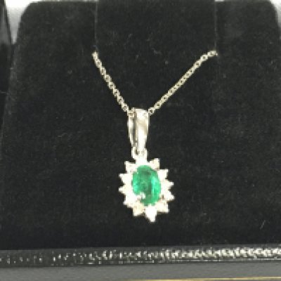 9ct white gold oval emerald and diamond cluster pendant on a 9ct white gold chain. Emerald 0.22ct and diamond 0.12ct.