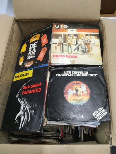 A box of 7" singles and EPs by various artists including Iron Maiden, Black Sabbath, The Mission, REM and many more.