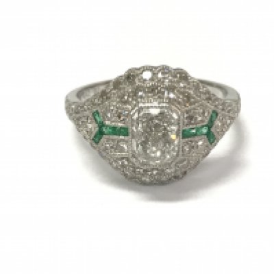 A platinum emerald and diamond ring with beaded finish and scroll design filigree sides. Central radiant cut diamond 0.42ct. Eight cut diamonds approximately 0.45ct. Calibre cut emeralds 0.10ct approximately. Size M.