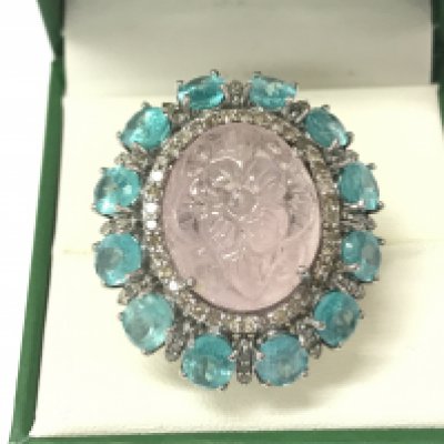 A large dress ring in white metal set with an oval carved morganite surrounded by oval apatites and diamonds. Morganite 19.18ct and apatities 10.26ct and 1.18ct diamonds approx. Size N