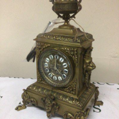 A brass cased late 19th century French clock the case surmounted with loin masks and ring ornamentation and surmounted with a classic urn. With side ornaments key and pendulum. Height 42cm