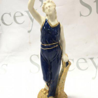 A Royal Worcester figure of Liberty standing wearing blue powdered dress edged in gilt standing on a rocky circular base , 24cm tall. This lot cannot be posted